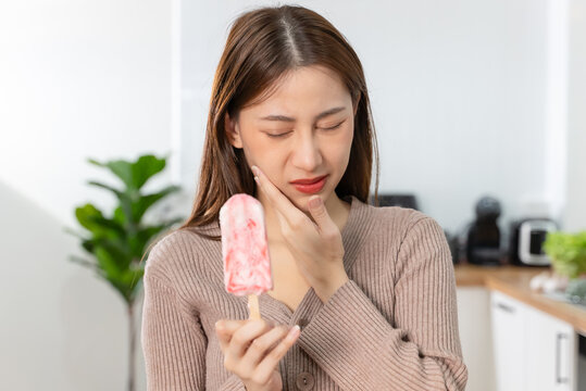 Asian Woman touching her chin feeling sensitive teeth when eating an ice cream. Have a gum and oral problem.