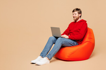 Full body young smart IT man he wear red hoodie casual clothes sit in bag chair hold use work on...