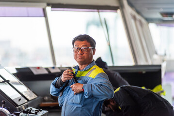 A marine engineer on the bridge of a large container ship, performing maintenance on navigation and communication equipment while the vessel is docked in port.