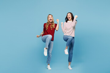 Fototapeta premium Full body young happy couple two friends women wear red casual clothes together do winner gesture celebrate clenching fists say yes raise up leg isolated on plain blue background. Lifestyle concept.
