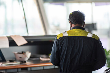 A person in a navy blue work uniform, a crew member a large cargo ship, during his work on the navigational bridge.