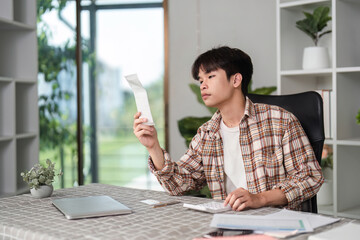 Young man thoughtfully analyzing a receipt in a modern home office.