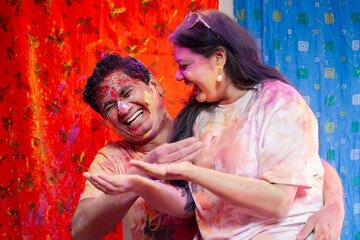 A playful and happy Indian couple is playing with vibrant Holi colors during the Indian festival of colors, Holi, which symbolizes love and tradition.