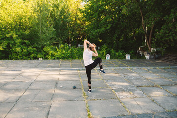 Fototapeta premium A woman is doing fitness outdoors. She is wearing a white T-shirt and black leggings.