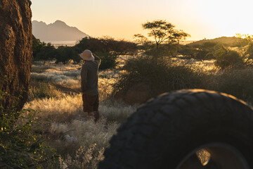 A safari explorer in the wilderness of Namibia around Spitzkoppe, watching the nature at sunset. 