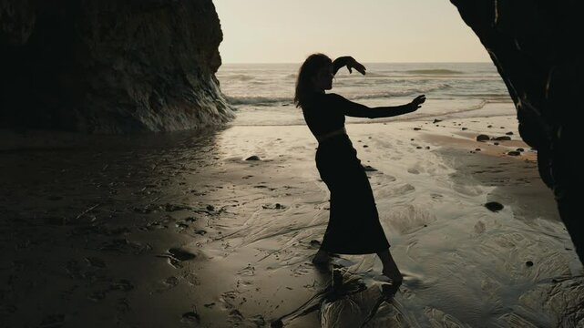 A graceful female dancer performs a silhouette dance on a serene beach at sunset, embodying freedom and elegance by the ocean shore.