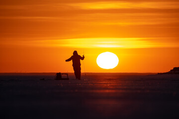 Fishermen on a frozen lake at sunset. Big sun