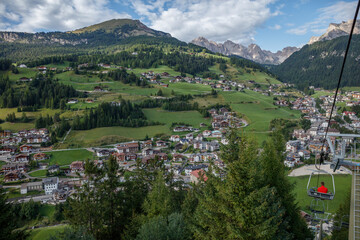 Fototapeta premium Spectacular view of the Dolomites from a ski lift during summer, showcasing the lush landscape and charming village below
