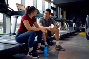 Personal trainer and female athlete talking during water break in gym.