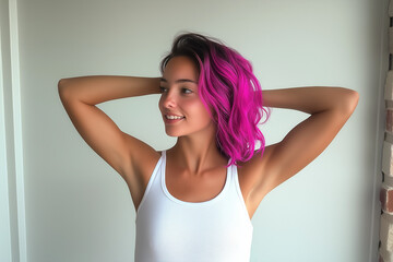 Fototapeta premium A girl with pink hair wearing a white tank top stretches her arms in a relaxed pose against a white studio background, exuding a sense of comfort and ease