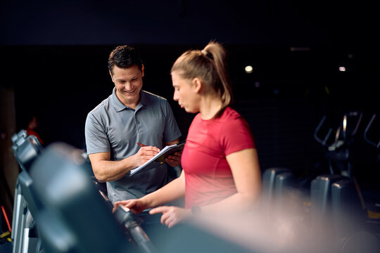 Happy fitness instructor taking notes during sportswoman's training in gym.