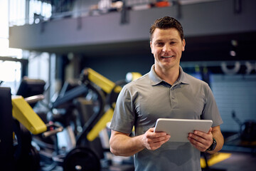 Happy personal coach with touchpad in gym looking at camera.