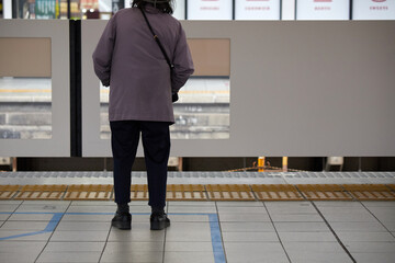 冬の朝の名古屋駅のホームで電車待ちのシニア女性の姿