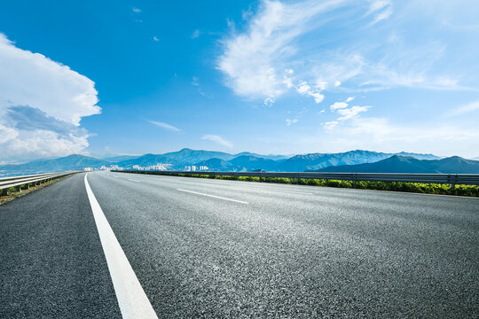 Empty asphalt road with mountain and city skyline under blue sky