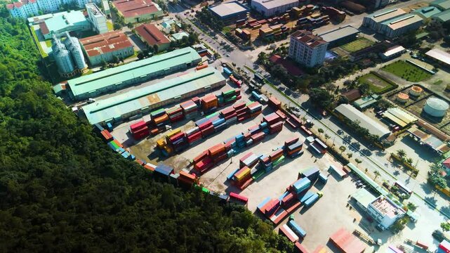 Industrial zone with colorful shipping containers bordering a forest, aerial view, showcasing logistics, transportation, and global trade in a vibrant urban setting