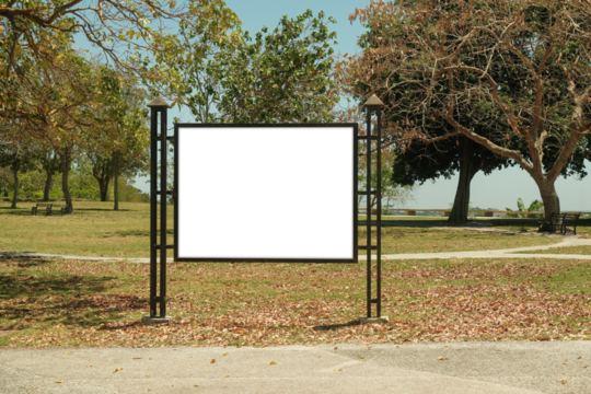 Mock up template: Horizontal billboard out of home (OOH) advertising poster in public park, Display held by iron metal frame design, installed on grass. Trees in background; bright sunny day.