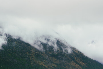 Low clouds are rising and covering the rocky mountain peaks, creating a mysterious and atmospheric landscape with lush green vegetation