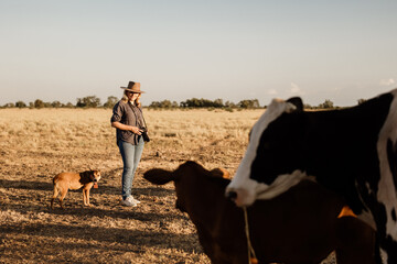 Woman standing in a dusty and dry grassy farm paddock holding a camera