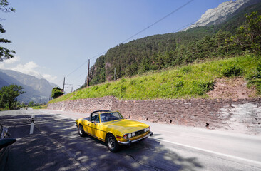 Vintage Yellow Car Driving on Scenic Mountain Road on a Sunny Day..