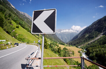 Mountain Road with Arrow Warning Sign in Scenic Alpine Landscape..