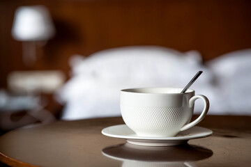 A white cup of hot tea or coffee on a wooden table in the interior of a hotel room. The concept of drinks and comfortable hotel accommodation.