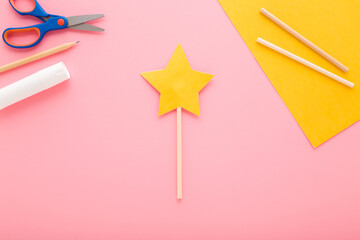 Yellow star magic wand created from application paper on light pink table background. Pastel color....