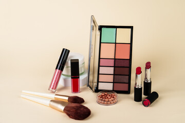 Makeup products. Eyeshadow palette, cream jar, lipsticks and brushes on colored background.