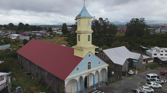 Aerial view capturing the vibrant Iglesia de Nuestra Senora del Rosario, surrounded by Chonchi's traditional wooden houses and lush greenery
