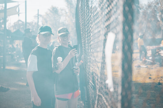 Teenagers watching vehicle burnout competition through chain mesh fence with smoke haze from burning