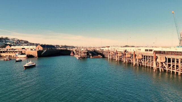 Low drone flight over water towards ferry berth and loading ramp St Peter Port Harbour Guernsey in brilliant late afternoon golden sunlight