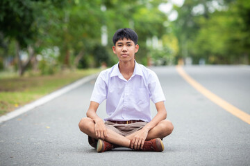 Thai country boy student in official Thai school uniform (khaki or brown shorts), properly dressed, sitting on the road
