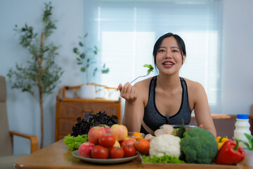 Beautiful asian sportswoman eating a portion of fresh salad in her modern and bright apartment, enjoying a healthy lifestyle and taking care of her body