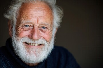 Elderly caucasian male with white beard smiling warmly against dark background.