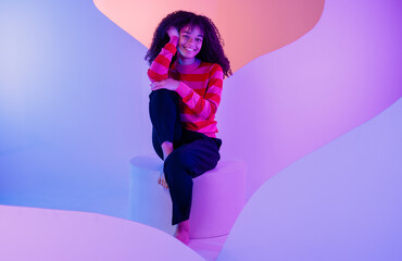 African in sweater sits at white round platform. Charming curly-haired woman in casual clothes