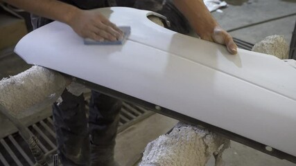 A worker sands a primed car fender in a body shop, preparing it for painting. Precision and craftsmanship in auto repair and finishing.