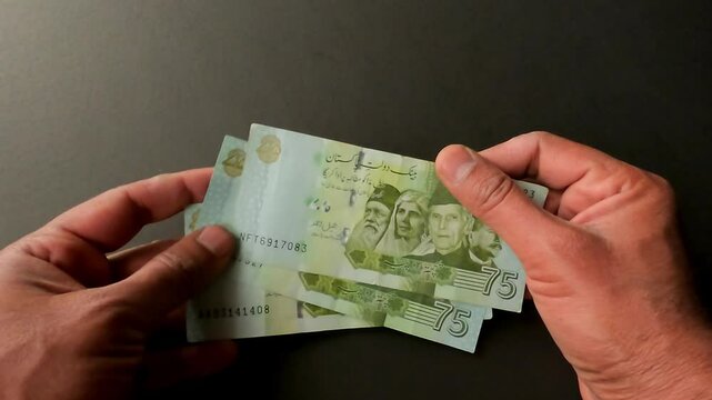 In commemoration of Pakistan's 75th Independence Day, a man is counting 75 rupee currency notes issued.