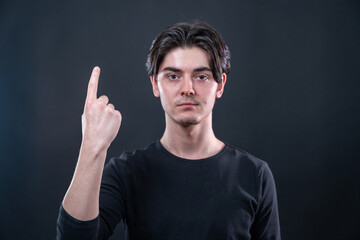 Portrait of a handsome young man showing his right index finger isolated on black background.