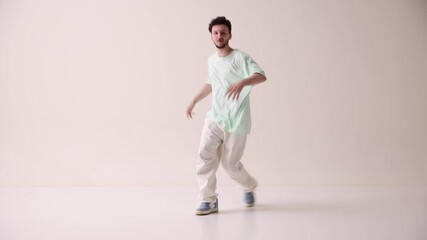 Young artistic man dressed casual, oversized stylish clothes dancing break dance in motion against white studio background. Concept of art and sport, music, creativity, fashion and style.