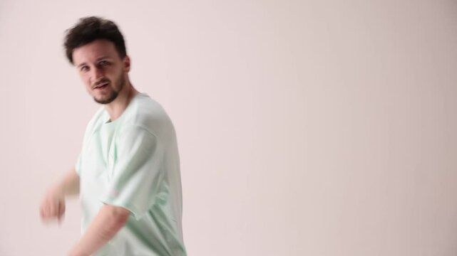 Young artistic man dressed casual, oversized stylish outfit dancing break dance in motion against white studio background. Concept of art and sport, music, creativity, fashion and style.