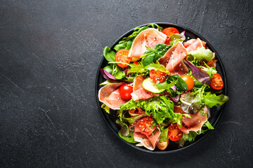 Green salad on black background. Green salad leaves, smoked meat and tomatoes. Top view with space for text.
