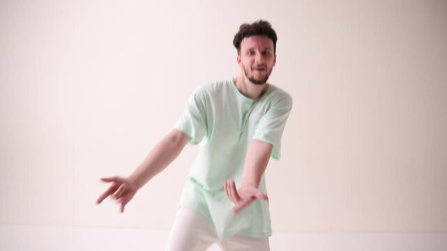Energetic, young, happy man dressed casual, oversized stylish outfit, dance freestyle in motion against white studio background. Concept of art and sport, music, creativity, fashion and style.