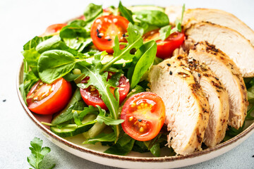 Healthy food. Green salad with grilled chicken meat at white table. Close up.