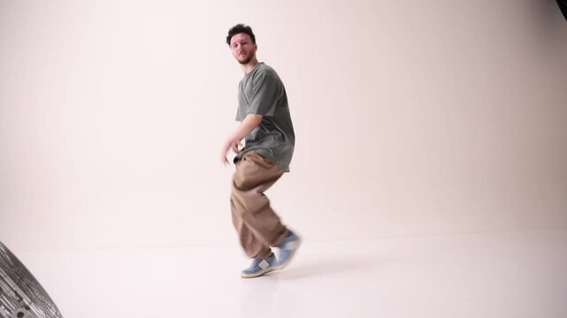 Cool attitude young man, talented freestyle dancer dancing in motion against white studio background. Concept of art and sport, music, creativity, fashion and style.