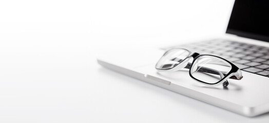 Closeup of an office table featuring a sleek laptop and reading glasses on a clean white surface