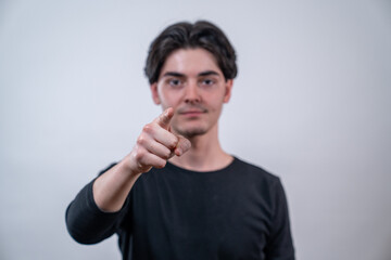 Serious young man pointing his finger at you isolated on white background. The focus is on the hand.