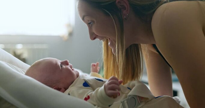 A caring mother face to face with her first child. Mom playing with son at home with natural light coming through the window. Infant smiling at mother.