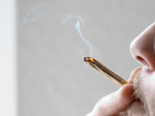 Smoking a joint close-up. Inhaling the smoke of a cigarette with cannabis. A young man is holding the glowing joint to his mouth and enjoying the taste and effect.