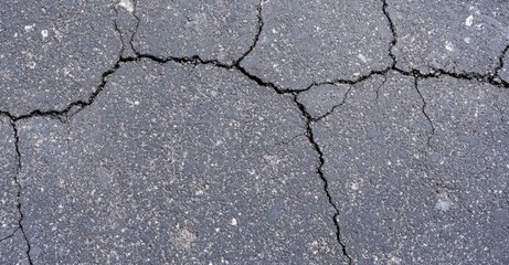 Obraz premium A close-up view of a cracked asphalt surface, highlighting various fissures and textures in the pavement.