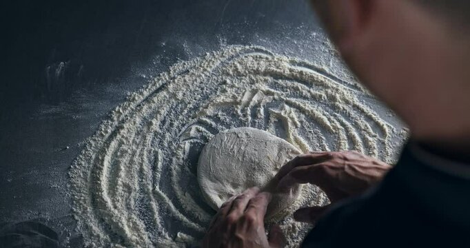 Top view of pizza maker making fresh pizza from a piece of dough. Experienced Chef kneading dough making fresh pasta. Pizzaiolo making food in bakery. Pizzeria restaurant making handmade pizza.