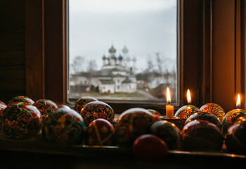 painted easter eggs and candles orthodox , at the window in Russian village home , ostern orthodox church in the background seen through the glass Happy Easter! Slavic religion